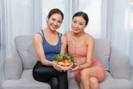 Téléchargez les photos : Jeunes femmes asiatiques sportives en vêtements de sport tenant saladier remplir ensemble avec vibrant de fruits et légumes. Style de vie corporel naturel jeune et en forme avec équilibre nutritionnel et exercice à la maison. Vigoureux - en image libre de droit