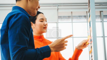 Photo for Business people work on project planning board in office and having conversation with coworker friend to analyze project development . They use sticky notes posted on glass to make it organized. Jivy - Royalty Free Image