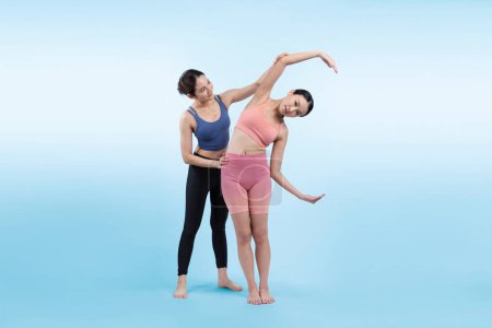 Photo for Asian woman in sportswear doing yoga exercise in standing pose with her trainer or yoga buddy. Healthy body care and meditation yoga lifestyle in full shot on isolated background. Vigorous - Royalty Free Image
