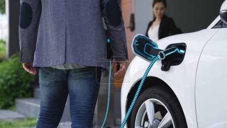 Photo for Modern family couple recharge electric car, EV charger from home charging station plugged in EV car in house garage. Smart and futuristic home energy infrastructure. Peruse - Royalty Free Image