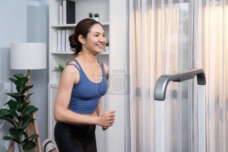 Photo for Energetic and strong athletic asian woman running running machine at home. Pursuit of fit physique and commitment to healthy lifestyle with home workout and training. Vigorous - Royalty Free Image