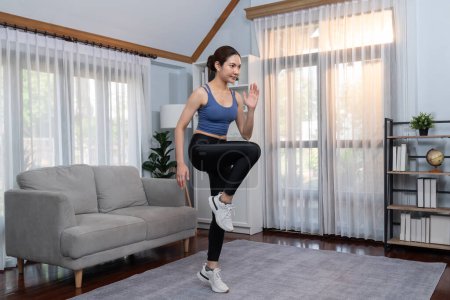 Foto de Enérgica y fuerte atlética mujer asiática corriendo en su lugar en su casa. Búsqueda de físico en forma y compromiso con un estilo de vida saludable con entrenamiento en casa y entrenamiento. Vigoroso - Imagen libre de derechos