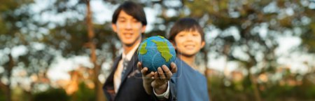 Téléchargez les photos : Focus panorama La Terre avec un garçon asiatique flou et un homme d'affaires tenant le globe ensemble comme concept de jour de la Terre. Responsabilité sociale des entreprises pour rendre l'environnement plus vert pour les générations futures durables. Pneumatique - en image libre de droit