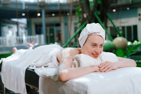 Photo for Beautiful young woman relaxes on a spa bed surrounded by nature. ready for a body massage. Attractive female in white towel lying peacefully during waiting for body massage. Close up. Tranquility - Royalty Free Image