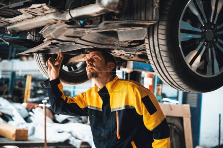 Photo for Vehicle mechanic conduct car inspection from beneath lifted vehicle. Automotive service technician in uniform carefully diagnosing and checking cars axles and undercarriage components. Oxus - Royalty Free Image