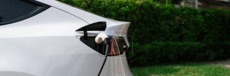 Photo for Closeup EV charger plug handle attached to electric vehicle port, recharging battery from charging station. Modern designed EV car and clean energy sustainability for better future.Panorama Synchronos - Royalty Free Image