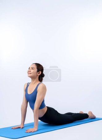 Téléchargez les photos : Femme asiatique en vêtements de sport faisant de l'exercice de yoga sur tapis de fitness comme sa routine d'entraînement d'entraînement. Soins du corps sains et méditation calme dans le mode de vie de yoga dans le corps entier tourné sur fond isolé. Vigoureux - en image libre de droit