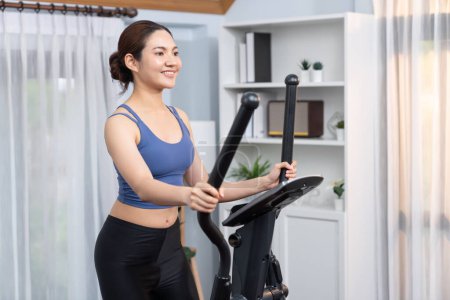 Photo for Energetic and strong athletic asian woman running on elliptical running machine at home. Pursuit of fit physique and commitment to healthy lifestyle with home workout and training. Vigorous - Royalty Free Image