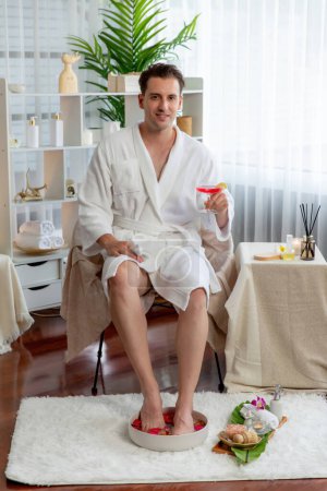 Photo for Beauty or body treatment spa salon vacation lifestyle concept with man wearing bathrobe relaxing with drinks in luxurious hotel spa or resort room. Vacation and leisure relaxation. Quiescent - Royalty Free Image