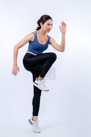 Photo for Side view young athletic asian woman on running posture in studio shot on isolated background. Pursuit of healthy fit body physique and cardio workout exercise lifestyle concept. Vigorous - Royalty Free Image