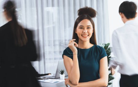 Photo for Young Asian businesswoman portrait poses confidently with diverse coworkers in busy meeting room in motion blurred background. Multicultural team works together for business success. Concord - Royalty Free Image
