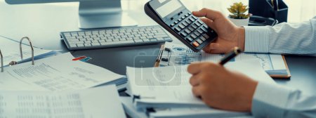 Photo for Corporate auditor calculating budget with calculator on his office desk. Dedicated accountant professional of accounting business company analyzing financial document to forecast income. Insight - Royalty Free Image