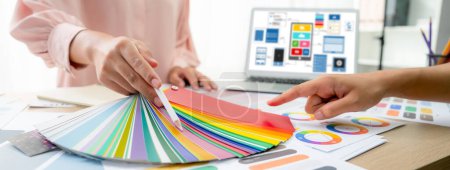 Photo for Cropped image of interior designer chooses color from color swatches while laptop displayed UI and UX designs for mobiles app and website. Creative design and business concept. Variegated. - Royalty Free Image