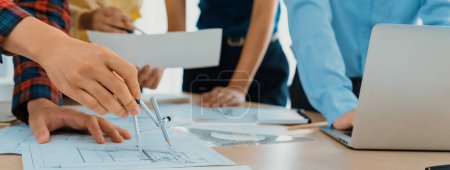 Photo for Architect team discuss about blueprint design at modern meeting room while her coworker working on laptop on table with blueprint and architectural equipment scattered around. Closeup. Delineation. - Royalty Free Image