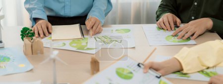 Photo for Green business meeting represented renewable energy. Skilled businesspeople discuss green business investment at table with environmental documents. Closeup. Focus on hand. Delineation. - Royalty Free Image