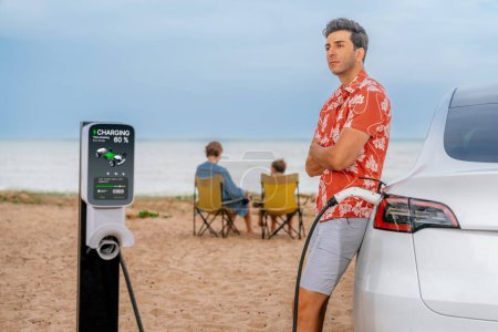 Photo for Family vacation trip traveling by the beach with electric car, dad or father recharge EV car while his family enjoy seascape beach. Family trip with alternative energy and eco-friendly car. Perpetual - Royalty Free Image