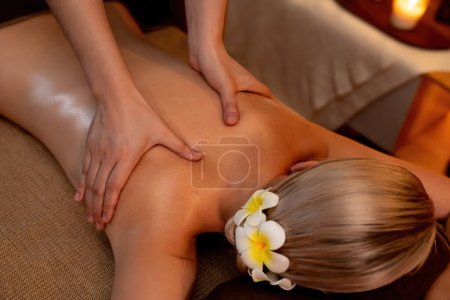 Photo for Closeup woman customer enjoying relaxing anti-stress spa massage and pampering with beauty skin recreation leisure in warm candle lighting ambient salon spa at luxury resort or hotel. Quiescent - Royalty Free Image