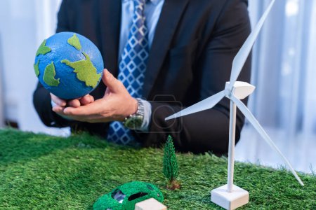 Téléchargez les photos : Eco business et sauver la Terre concept montré par l'homme d'affaires ou PDG tenant globe de papier en fonction avec une maquette écologique pour promouvoir la réduction de CO2 et de l'empreinte carbone pour un avenir plus vert. Charmante. - en image libre de droit