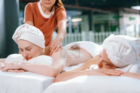 Foto de Un par de hermosas mujeres jóvenes yacen en la cama de spa blanca durante el masaje de espalda. Atractiva mujer caucásica que tiene masaje de espalda en la sala de spa tradicional. Relajante y concepto saludable Tranquilidad. - Imagen libre de derechos
