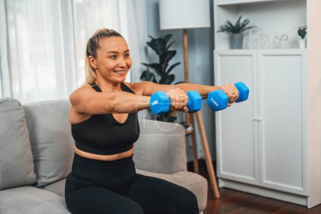 Photo for Athletic and sporty senior woman engaging in body workout routine with lifting dumbbell at home as concept of healthy fit body with body weight lifestyle after retirement. Clout - Royalty Free Image