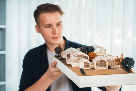 Photo for Architect designer studies elegant while holding house model, reviewing structure design for improvement with construction plan on table. Creativity and innovation in architectural design. Iteration - Royalty Free Image