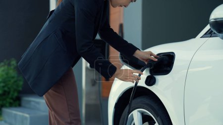 Téléchargez les photos : Une femme progressiste installe une borne de recharge dans son véhicule électrique à la maison. EV automobiles fournissent un concept écologique bénéfique d'énergie propre et verte. - en image libre de droit