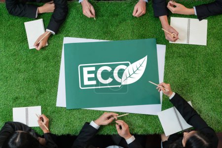 Téléchargez les photos : Top view panoramique ECO symbole sur la table d'herbe verte avec les gens d'affaires qui envisagent une utilisation alternative de l'énergie pour une Terre plus verte et durable en tant que responsabilité sociale des entreprises. Charmante. - en image libre de droit