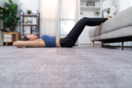 Foto de Fondo borroso de joven atractiva mujer asiática en ropa deportiva se encuentra en el suelo de la casa y hacer abdominales en el agacharse, ayudando a la orientación en el músculo abdominales para la rutina de ejercicio en casa eficaz. Vigoroso - Imagen libre de derechos