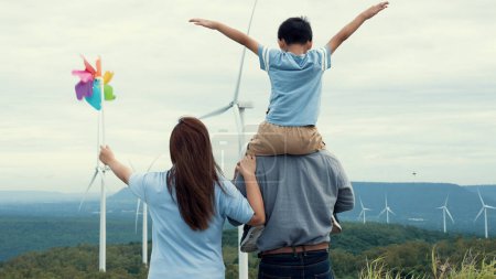 Téléchargez les photos : Concept de famille heureuse progressive appréciant leur temps au parc d'éoliennes. Générateur électrique à partir du vent par éolienne sur le côté campagne avec colline et montagne à l'horizon. - en image libre de droit