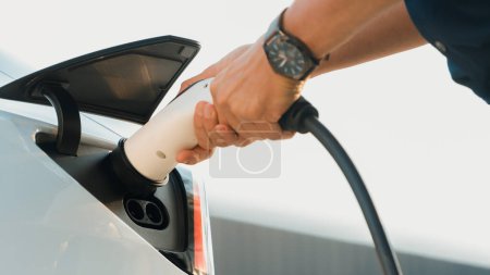 Photo for Closeup hand put EV charger to recharge electric cars battery from charging station in city commercial parking lot. Rechargeable EV car for sustainable environmental friendly urban travel. Expedient - Royalty Free Image