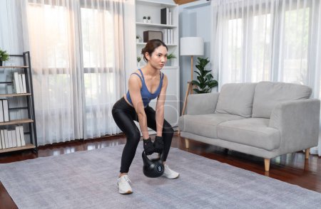 Photo for Vigorous energetic woman doing squat with kettlebell weight lifting exercise at home. Young athletic asian woman strength and endurance training session as home workout routine. - Royalty Free Image