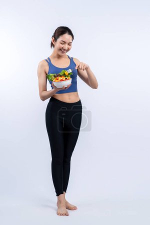 Foto de Joven mujer asiática deportiva en ropa deportiva sosteniendo ensaladera llenar con vibrante de frutas y verduras. Estilo de vida corporal joven y en forma natural con nutrición de equilibrio sobre un fondo aislado. Vigoroso - Imagen libre de derechos