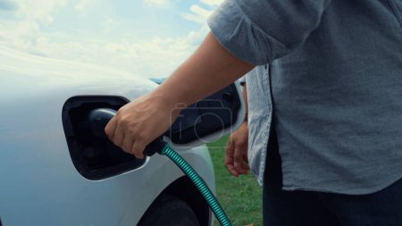 Photo for Hand insert EV charger and recharge electric car from charging station on nature and travel concept background. Technological advancement of alternative energy sustainability and EV car. Peruse - Royalty Free Image