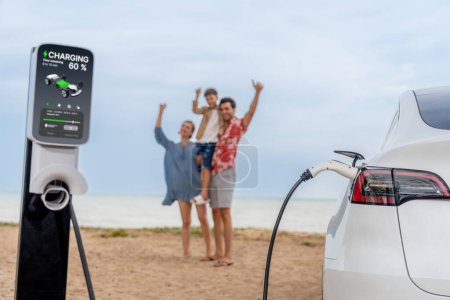 Photo for Alternative family vacation trip traveling by the beach with electric car recharging battery from EV charging station with blurred cheerful and happy family enjoying the seascape background. Perpetual - Royalty Free Image