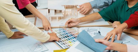 Photo for Skilled architect team discuss about house construction while interior designer point an appropriate color on color palette with house model and blueprint scatter around. Top view. Variegated. - Royalty Free Image