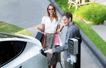 Photo for Young couple travel with EV electric car charging in green sustainable city outdoor garden in summer shows urban sustainability lifestyle by green clean rechargeable energy of electric vehicle innards - Royalty Free Image