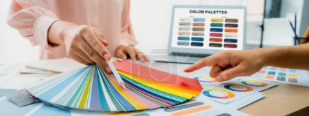 Photo for Cropped imaged of professional interior designers choose appropriate color from color palette with house model and architectural equipment scatter around. Closeup. Focus on hand. Variegated. - Royalty Free Image