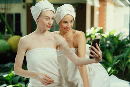 Téléchargez les photos : Couple de jeunes belles femmes avec une belle peau en serviette blanche prenant une photo ensemble à l'extérieur entouré d'un environnement naturel paisible. Beauté et concept de spa sain. Tranquillité. - en image libre de droit
