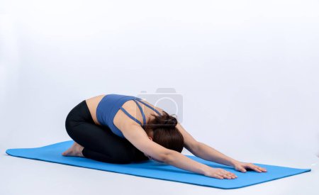 Téléchargez les photos : Femme asiatique en vêtements de sport faisant de l'exercice de yoga sur tapis de fitness comme sa routine d'entraînement d'entraînement. Soins du corps sains et méditation calme dans le mode de vie de yoga dans le corps entier tourné sur fond isolé. Vigoureux - en image libre de droit