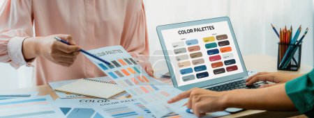 Photo for Creative graphic design presents selective color while manager using laptop comparing suitable color at table with color palettes, graphic material scatter around at modern office. Variegated. - Royalty Free Image