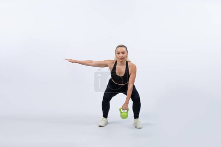 Photo for Full body length shot athletic and sporty senior woman doing squat with kettlebell for body workout on isolated background. Healthy active physique and body care lifestyle after retirement. Clout - Royalty Free Image