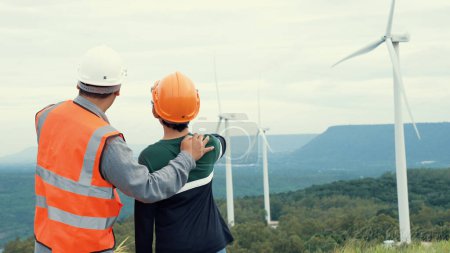 Photo for Engineer with his son on a wind farm atop a hill or mountain in the rural. Progressive ideal for the future production of renewable, sustainable energy. Energy generation from wind turbine. - Royalty Free Image