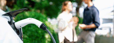 Téléchargez les photos : Jeune couple recharger la batterie de voiture électrique de la station de charge dans le parc vert de la ville au printemps. Voiture rechargeable pour un mode de vie urbain durable et respectueux de l'environnement. Panorama Expedient - en image libre de droit
