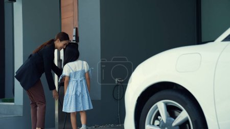 Photo for Progressive lifestyle of mother and daughter who have just returned from school in an electric vehicle that is being charged at home. Electric vehicle powered by sustainable clean energy. - Royalty Free Image