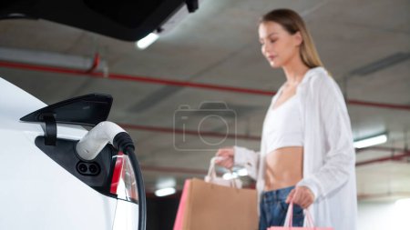 Photo for Young woman travel with EV electric car to shopping center parking lot charging in downtown city showing urban sustainability lifestyle by green clean rechargeable energy of electric vehicle innards - Royalty Free Image
