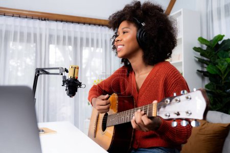 Photo for Host channel of beautiful African woman influencer singing with playing guitar in broadcast studio. Time slot of music blogger on live social media online. Concept of audio creator. Tastemaker. - Royalty Free Image
