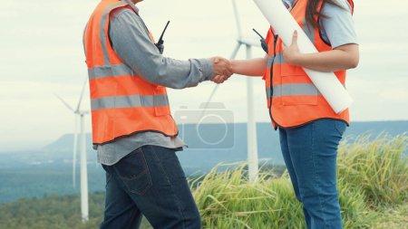 Foto de Ingenieros masculinos y femeninos trabajando en un parque eólico en lo alto de una colina o montaña en el campo. Ideales progresivos para la producción futura de energía renovable y sostenible. - Imagen libre de derechos