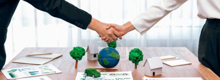 Photo for Business people shake hand over table with Eco concept mockup after made successful agreement deal on environmental conservation and sustainable energy matters to reduce CO2 emission. Trailblazing - Royalty Free Image