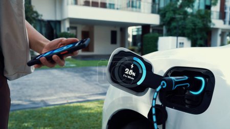 Photo for Modern woman recharge her EV car from home charging station by EV charger, checking battery status from EV smartphone app. Future lifestyle of sustainable clean energy utilization. Peruse - Royalty Free Image