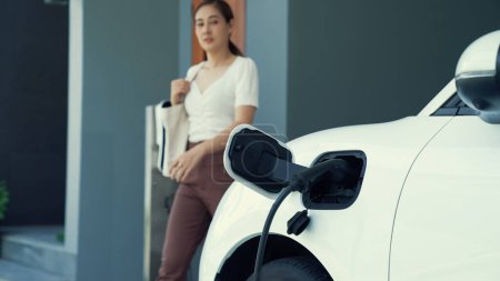 Photo for A woman unplugs the electric vehicles charger at his residence. Concept of the use of electric vehicles in a progressive lifestyle contributes to a clean and healthy environment. - Royalty Free Image